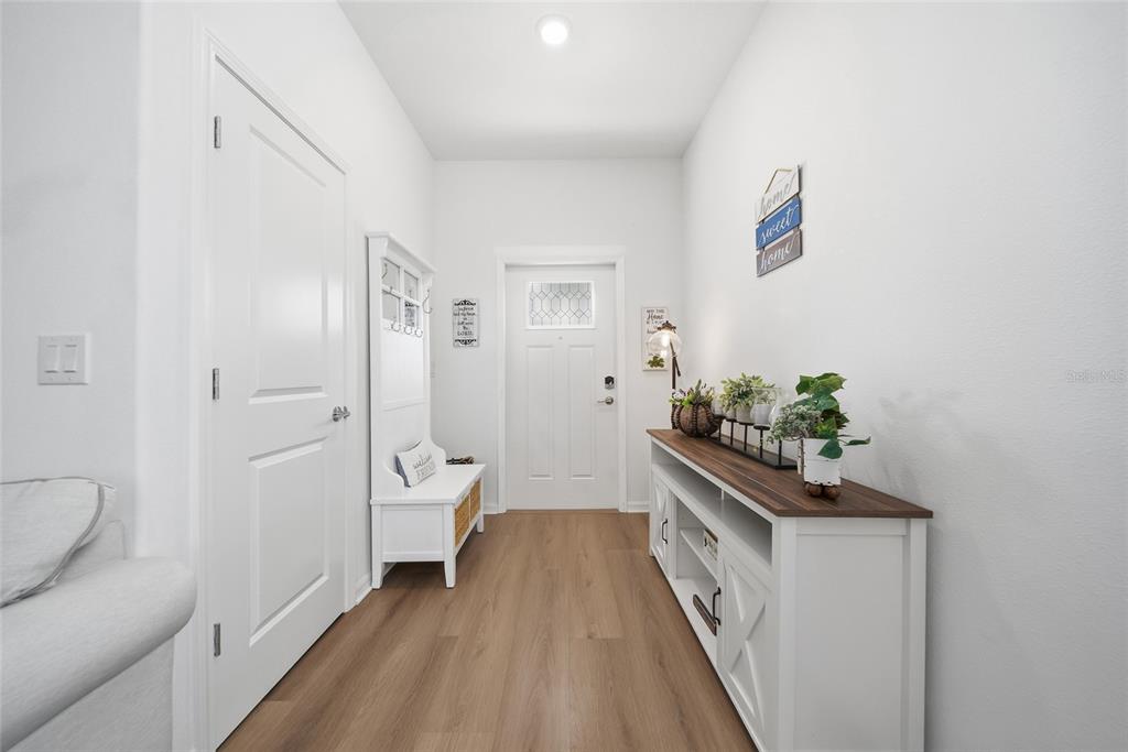A bright entryway features light wood-look flooring, a white console table, and a hall tree — 32041 POWDERPUFF MIMOSA DRIVE, SAN ANTONIO, FL