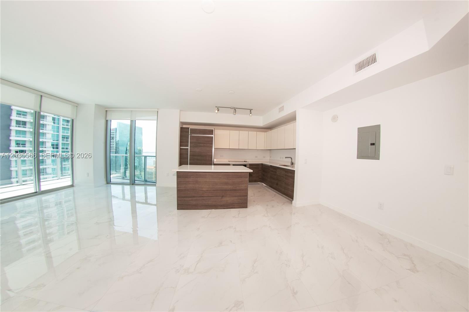 A modern kitchen with wood-toned cabinetry and a white island sits in an open-plan room — 1100 S MIAMI AV # 4001, Miami FL 33130, MIAMI, FL