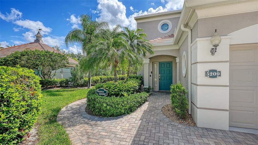 A paved walkway leads to the teal front door of a house with beige siding — 5211 PARISIENNE PLACE UNIT 101B27, SARASOTA, FL