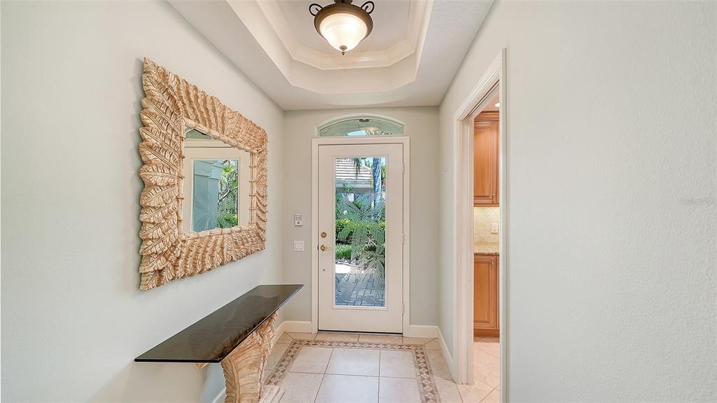An entryway features a glass-topped console table, a decorative mirror, and a glass-paneled front door — 5211 PARISIENNE PLACE UNIT 101B27, SARASOTA, FL