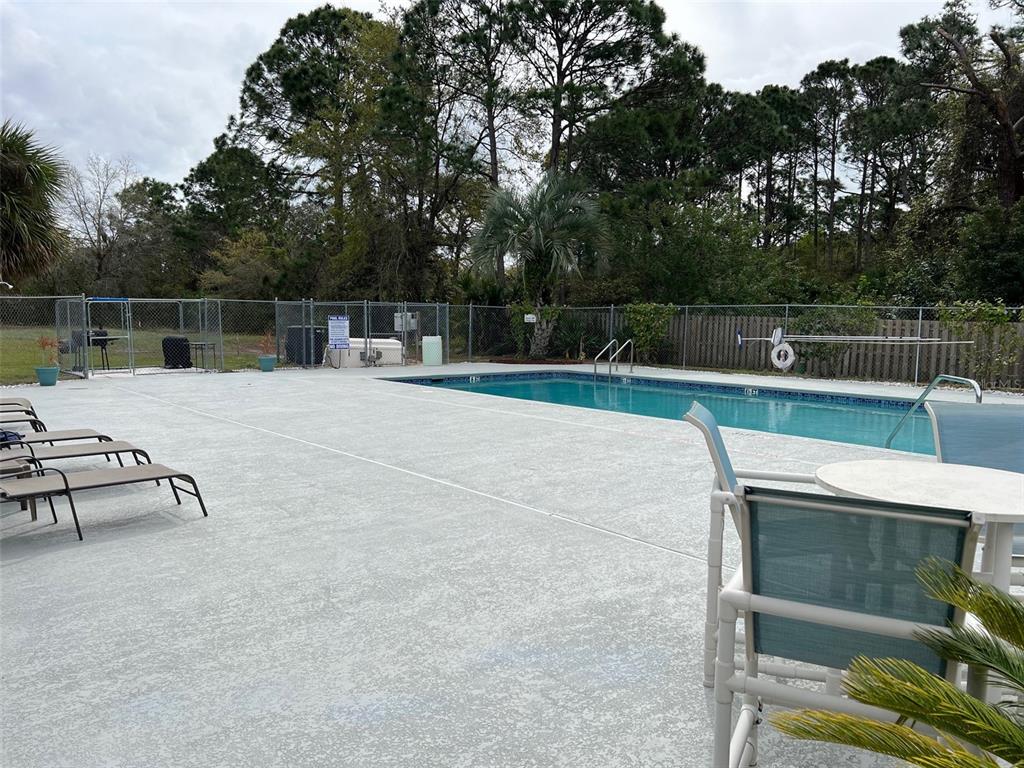 An outdoor swimming pool surrounded by a concrete deck, lounge chairs, and a chain-link fence — 1795 HARRISON STREET UNIT 215, TITUSVILLE, FL