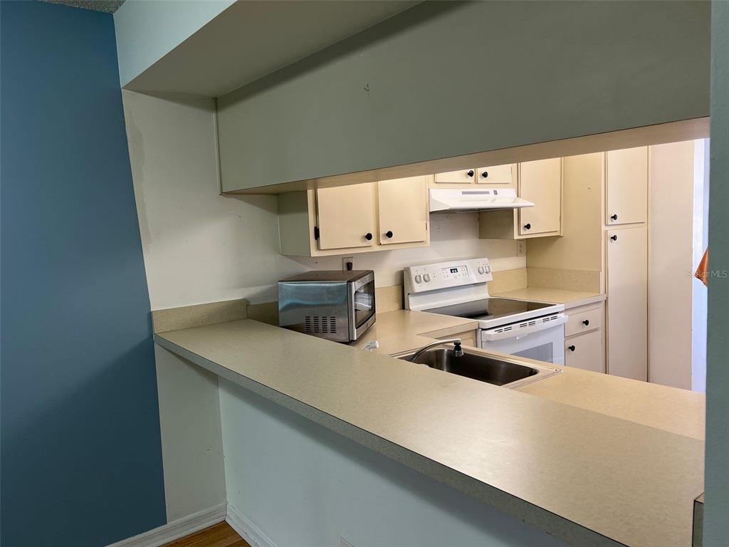 A kitchen features a pass-through counter, light-colored cabinets, a stainless steel microwave, and white appliances — 1795 HARRISON STREET UNIT 215, TITUSVILLE, FL
