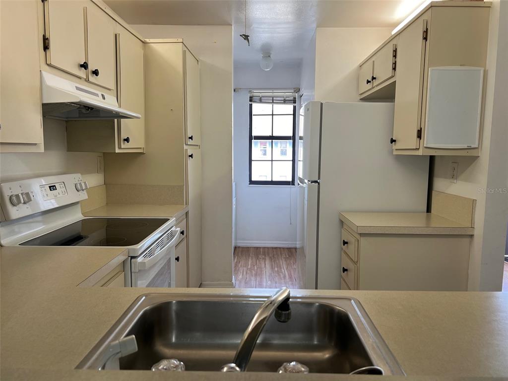 A galley kitchen features white cabinets, laminate countertops, a stainless steel sink, and white appliances — 1795 HARRISON STREET UNIT 215, TITUSVILLE, FL