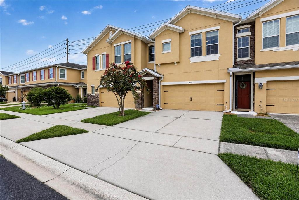 A row of two-story tan townhouses features attached garages, concrete driveways, and small front lawns — 1608 MOHEGAN BOULEVARD, KISSIMMEE, FL