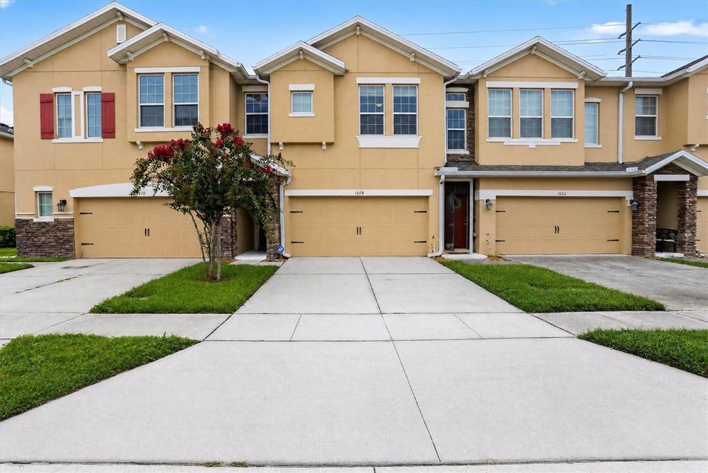 A row of three tan townhouses with attached garages and concrete driveways under a blue sky — 1608 MOHEGAN BOULEVARD, KISSIMMEE, FL