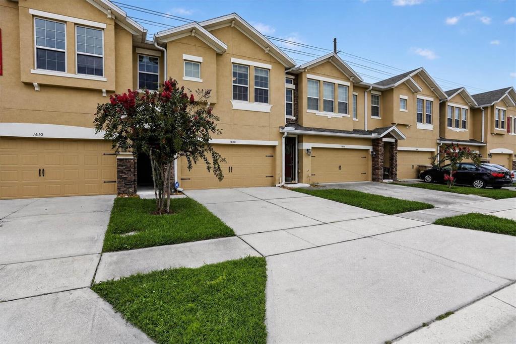 A row of tan townhouses with attached garages and concrete driveways under a blue sky — 1608 MOHEGAN BOULEVARD, KISSIMMEE, FL