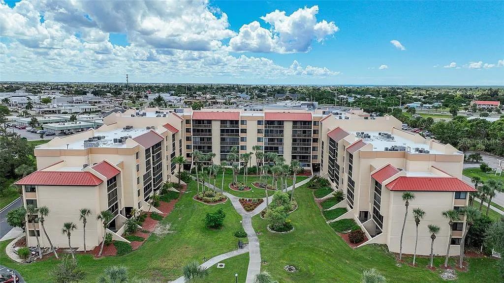An aerial view of a multi-story apartment complex with red roofs and a central courtyard — 3006 CARING WAY UNIT 329, PORT CHARLOTTE, FL