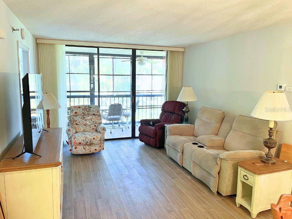 A living room features a beige sofa, two recliners, a television, and a sliding glass door — 3006 CARING WAY UNIT 329, PORT CHARLOTTE, FL