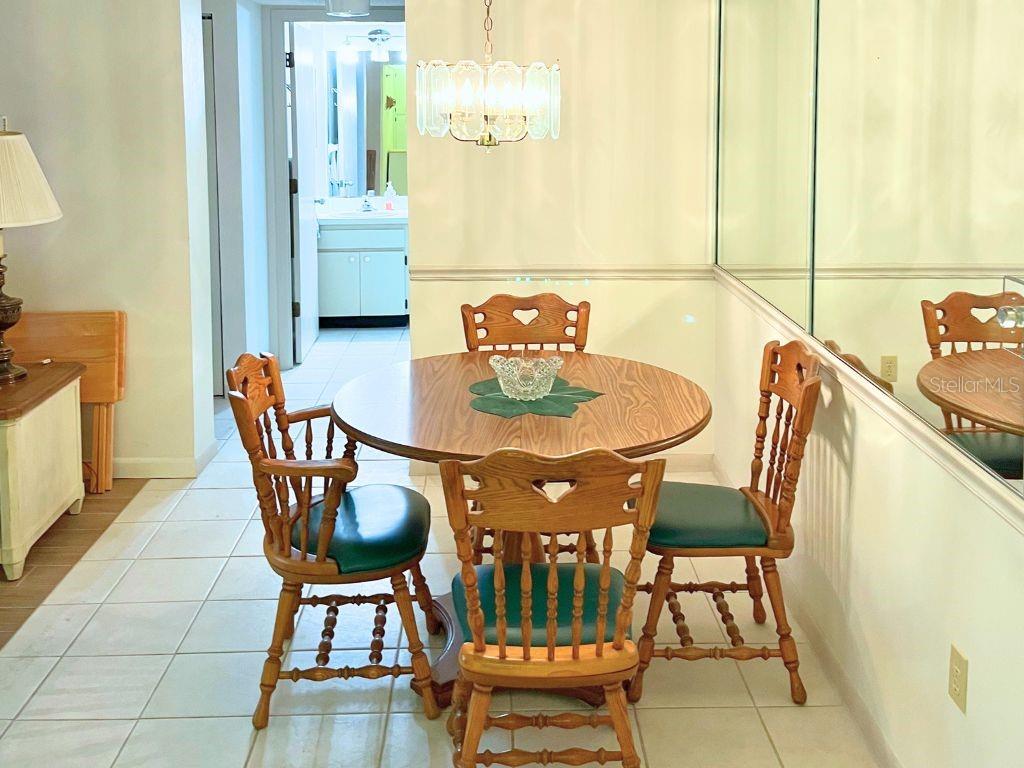 A living and dining area features a beige armchair, a round wooden table, and mirrored walls — 3006 CARING WAY UNIT 329, PORT CHARLOTTE, FL