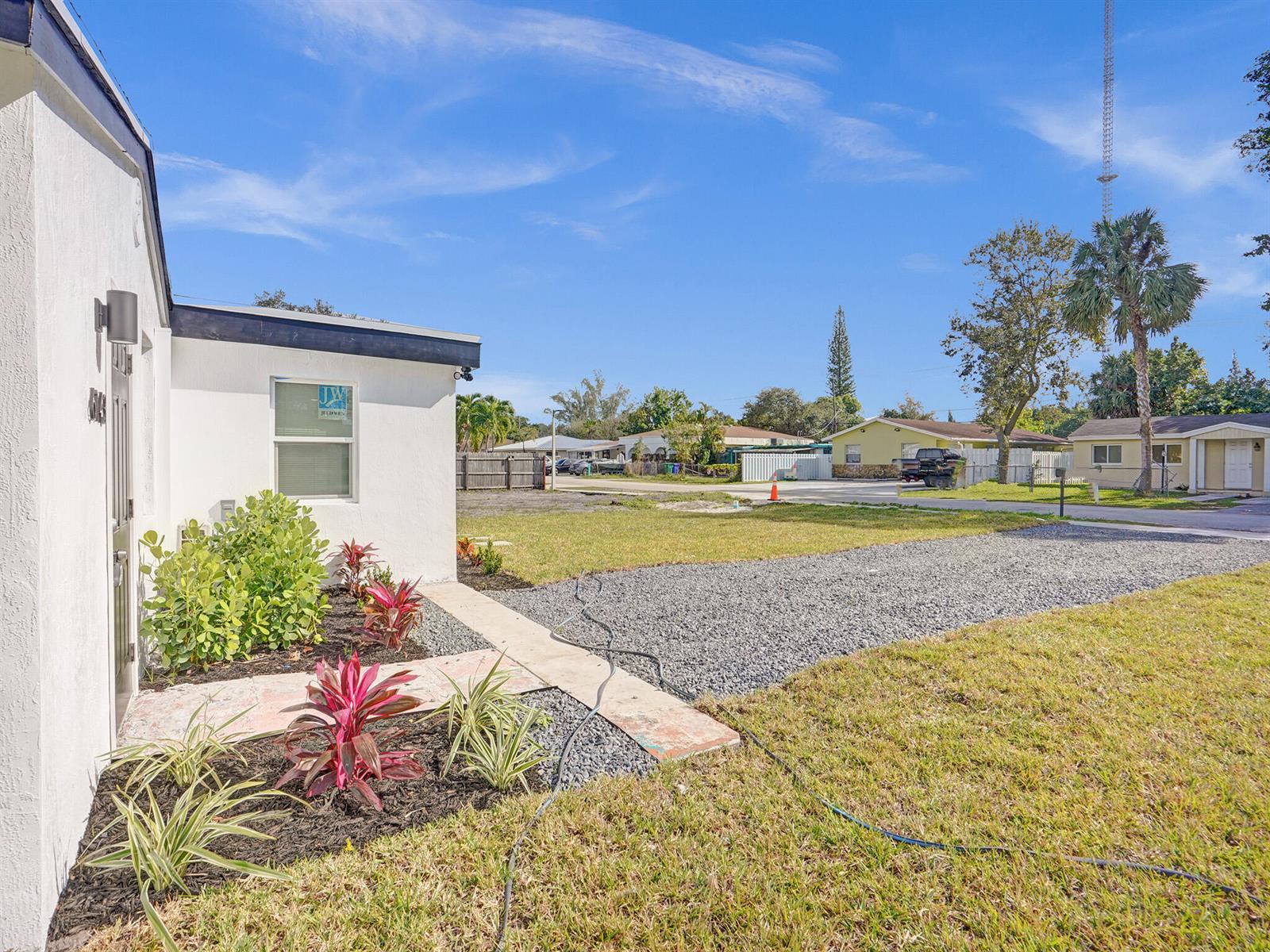 A white house exterior features a gravel driveway, a small garden bed, and a walkway — 6143 SW 40th Street, Miramar FL 33023, MIRAMAR, FL