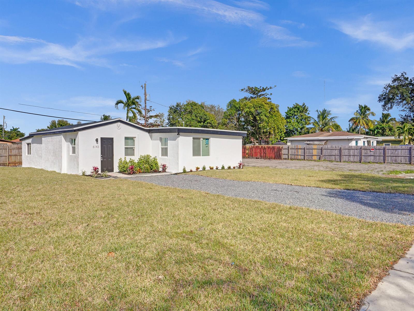 A white single-story house with a gravel driveway and a fenced yard under a blue sky — 6143 SW 40th Street, Miramar FL 33023, MIRAMAR, FL