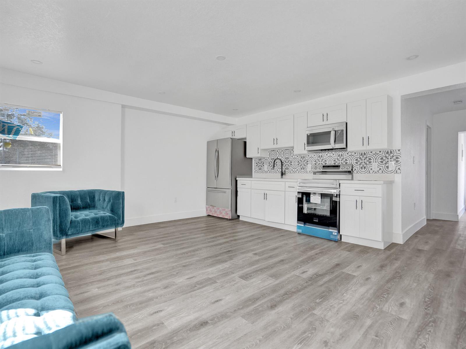 A kitchen with white cabinets, stainless steel appliances, and patterned backsplash opens to a living area — 6143 SW 40th Street, Miramar FL 33023, MIRAMAR, FL