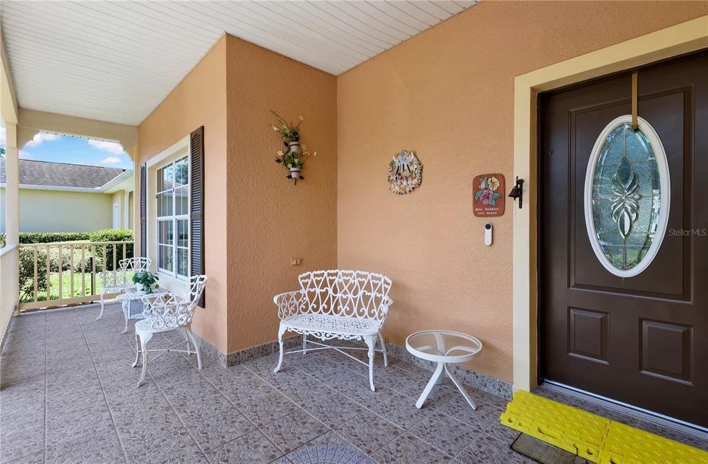 A covered front porch features tiled flooring, white metal furniture, and a brown front door — 362 LAKE CASSIDY DRIVE, POINCIANA, FL