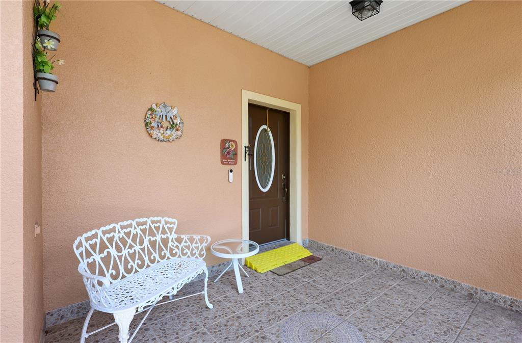 A covered front porch features a white metal bench, a small table, and a brown door — 362 LAKE CASSIDY DRIVE, POINCIANA, FL