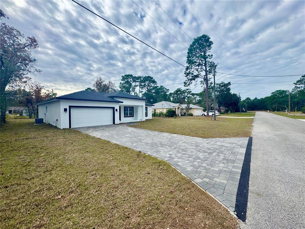 A white single-story house with a black roof and a paved driveway faces a road — 3284 W GATES LANE, CITRUS SPRINGS, FL