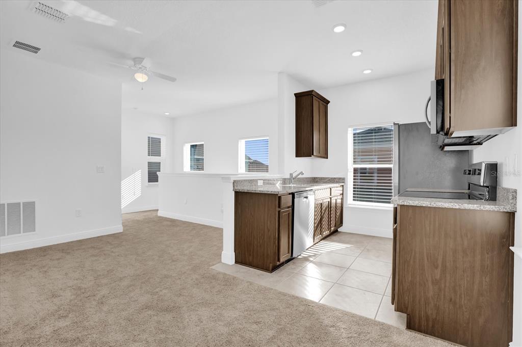A kitchen with dark wood cabinets and granite countertops opens into a carpeted living area — 3008 MIRAGE PLACE, ST CLOUD, FL