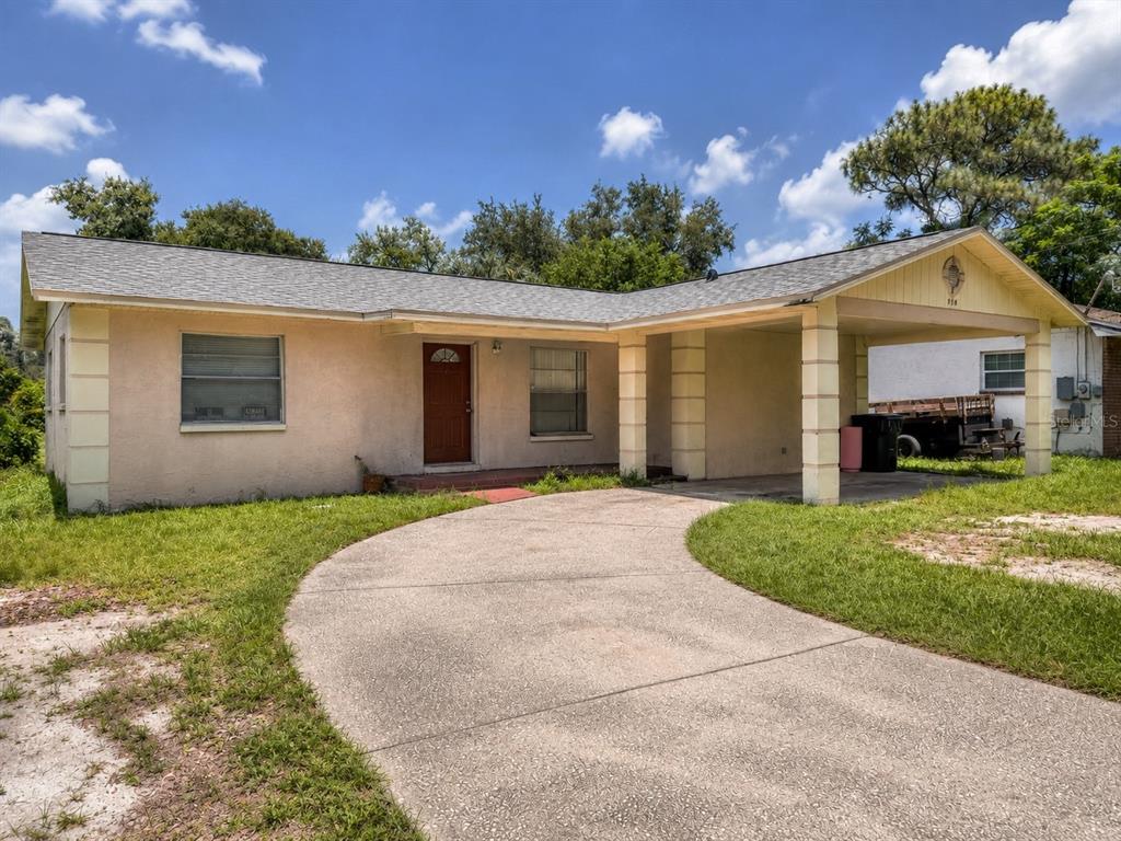 A single-story house with a beige stucco exterior, a red front door, and a carport — 1918 E HANNA AVENUE, TAMPA, FL