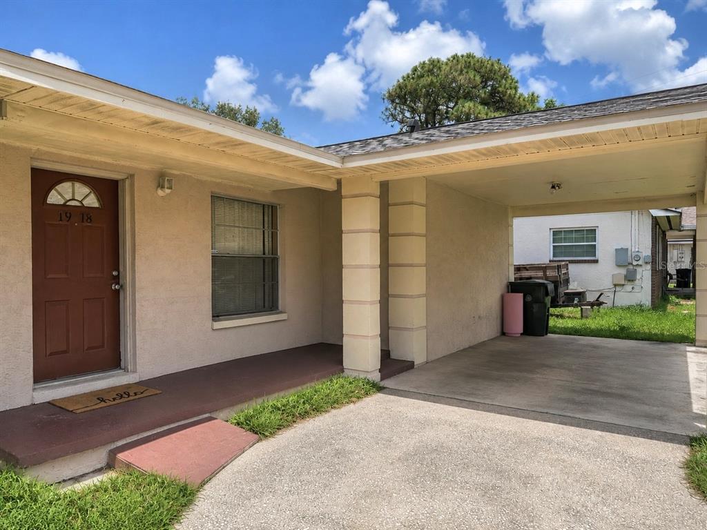 A single-story house exterior features a brown front door, a concrete carport, and stucco siding — 1918 E HANNA AVENUE, TAMPA, FL