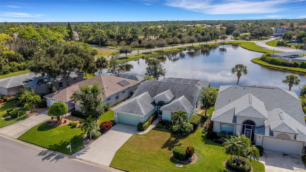 An aerial view shows three suburban houses with gray roofs situated along a small lake — 8976 WHITEMARSH AVENUE, SARASOTA, FL