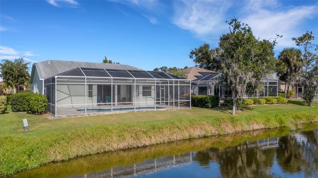A rear view of a house with a screened-in pool enclosure overlooking a small canal — 8976 WHITEMARSH AVENUE, SARASOTA, FL