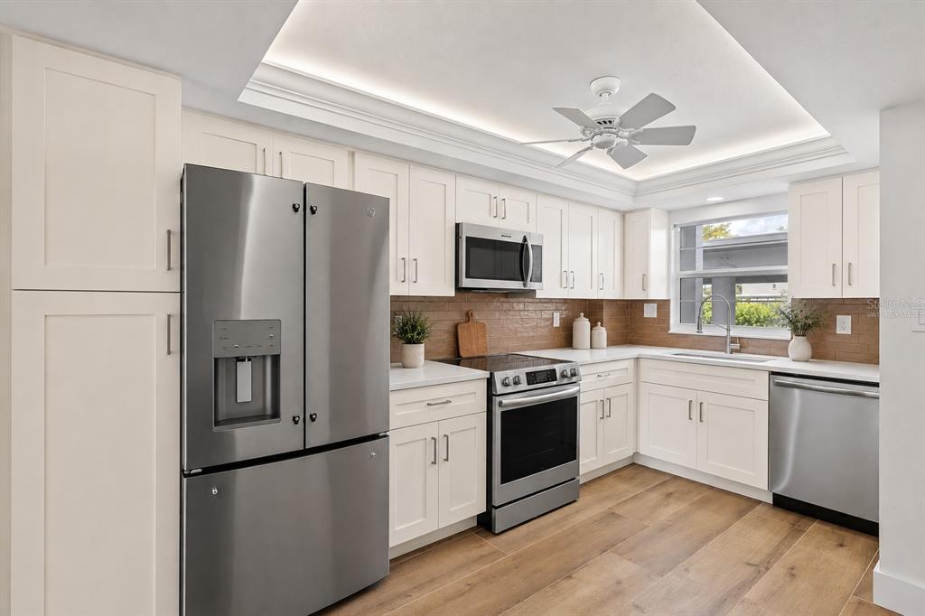 A kitchen with white cabinets, stainless steel appliances, wood-look flooring, and a brown tiled backsplash — 5600 BEACH WAY DRIVE UNIT 111, SARASOTA, FL