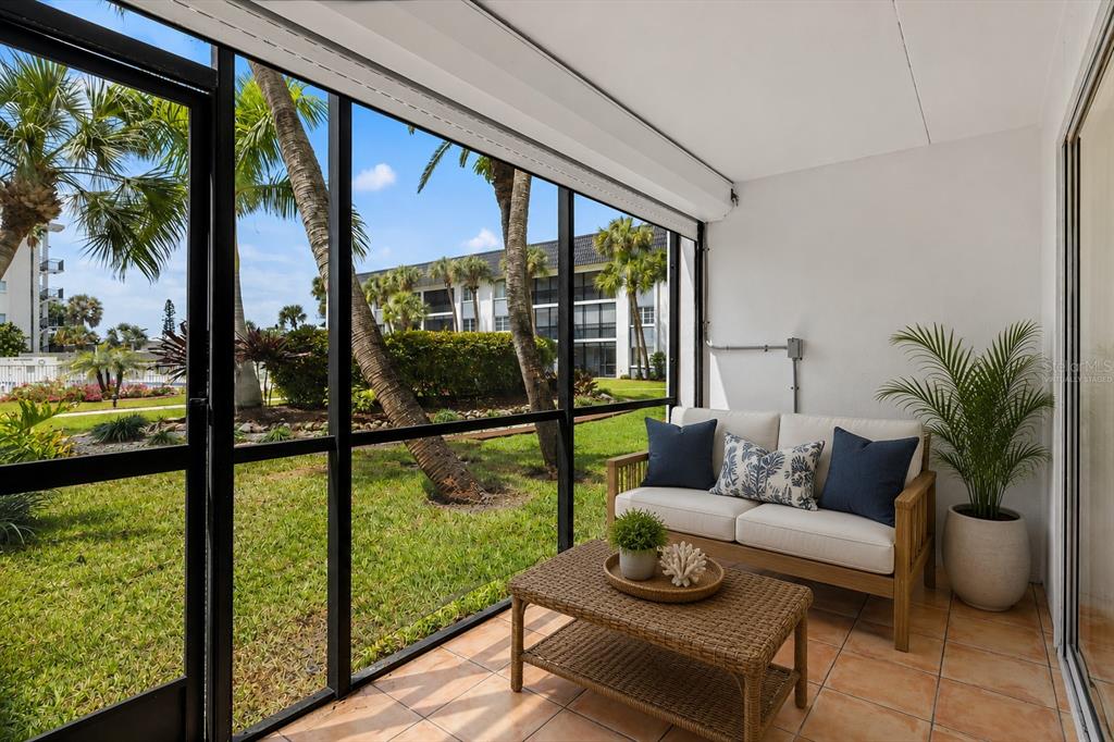 A screened-in patio with tile flooring, a wicker coffee table, and a sofa overlooking grass — 5600 BEACH WAY DRIVE UNIT 111, SARASOTA, FL