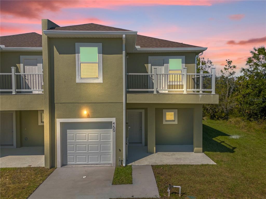 A two-story townhouse exterior features a single-car garage, a second-floor balcony, and a concrete driveway — 450 LAKE SHORE PARKWAY, DAVENPORT, FL
