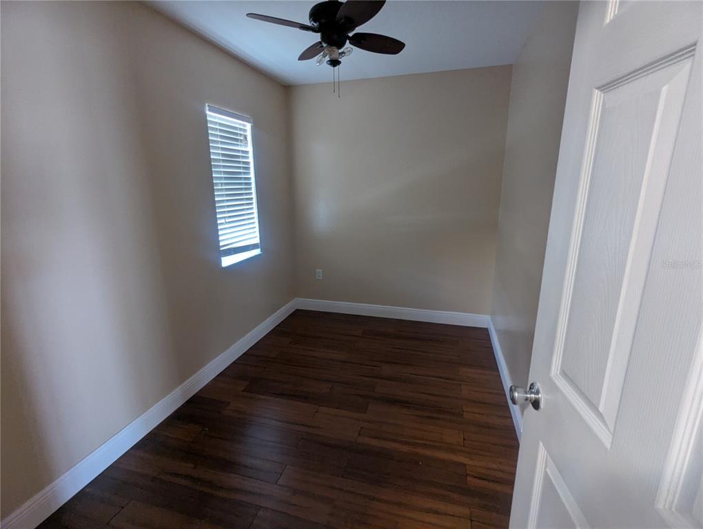 An empty bedroom features dark wood flooring, beige walls, a ceiling fan, and a window — 1628 STRTHMORE CIRCLE, MOUNT DORA, FL