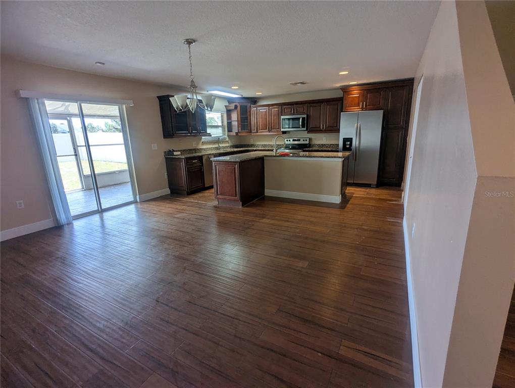 A kitchen with dark wood cabinets, stainless steel appliances, and wood-look flooring opens to a patio — 1628 STRTHMORE CIRCLE, MOUNT DORA, FL