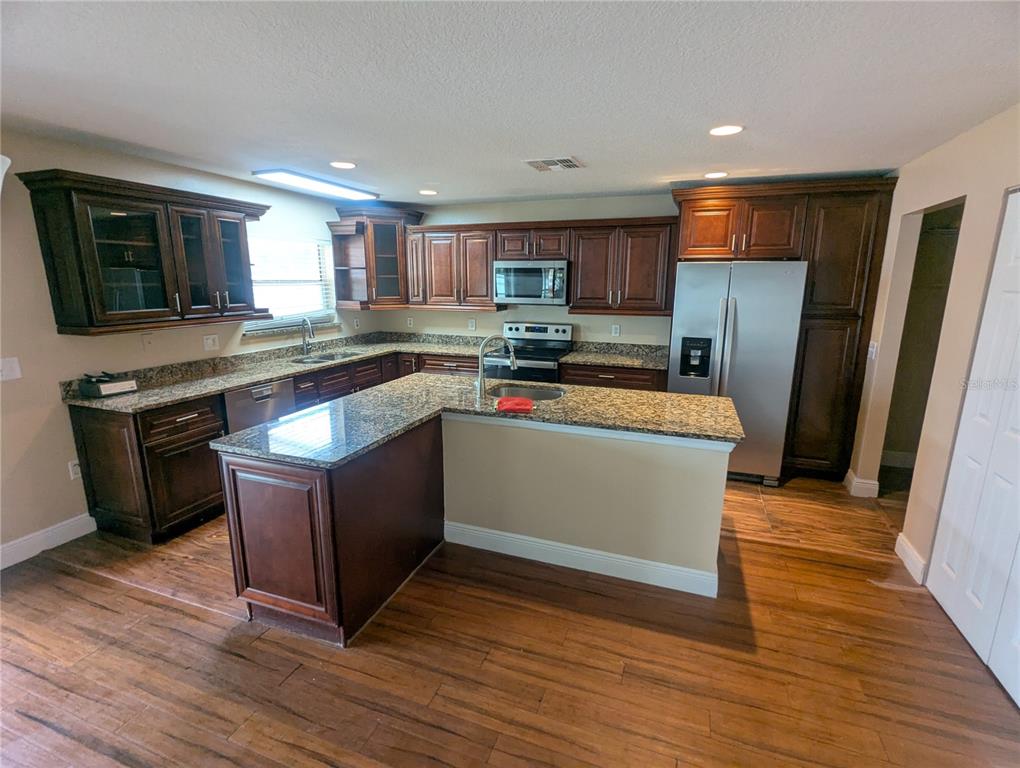 A kitchen features dark wood cabinets, granite countertops, stainless steel appliances, and wood-look flooring — 1628 STRTHMORE CIRCLE, MOUNT DORA, FL