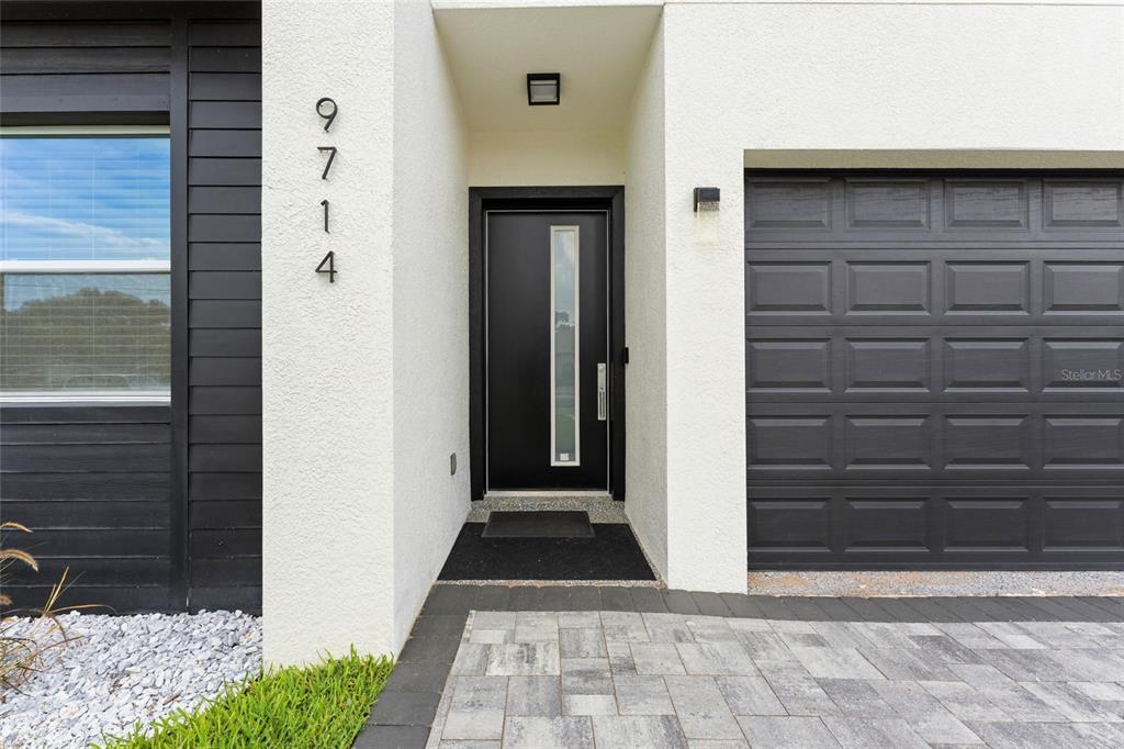 A modern home exterior features a black front door, a garage, and white stucco walls — 9714 VAN STREET, TAMPA, FL