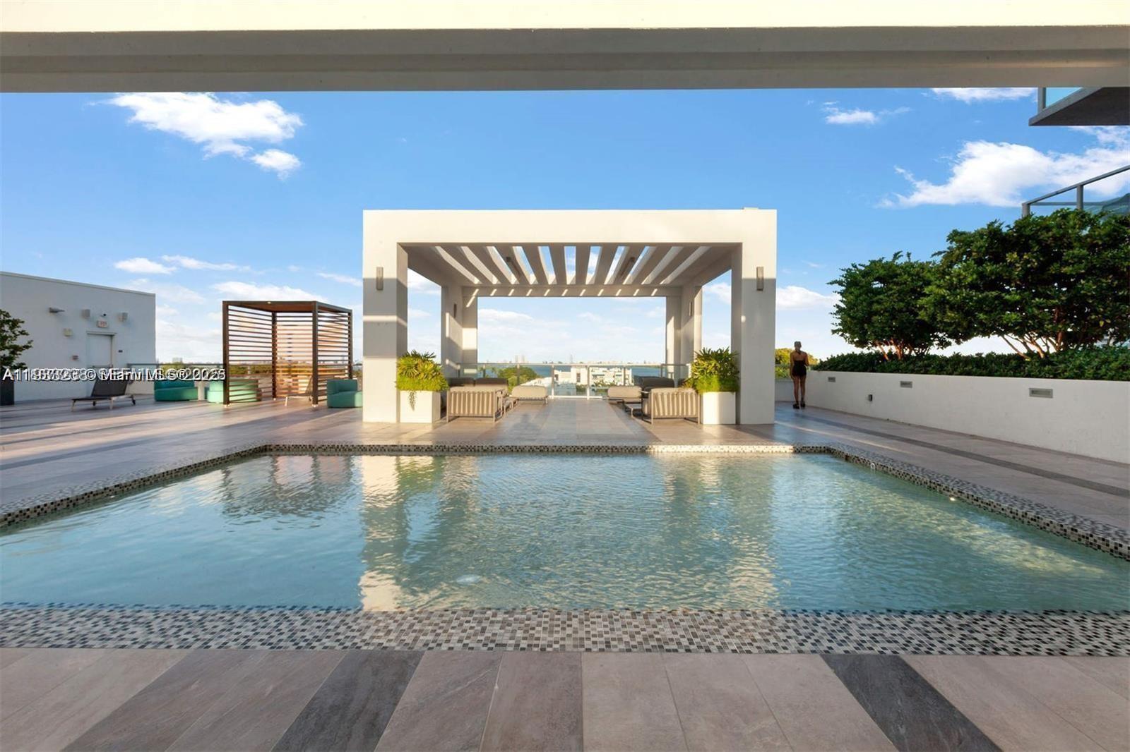 A rooftop swimming pool features a white pergola and lounge seating under a blue sky — 3900 Biscayne Blvd # 905, Miami FL 33137, MIAMI, FL