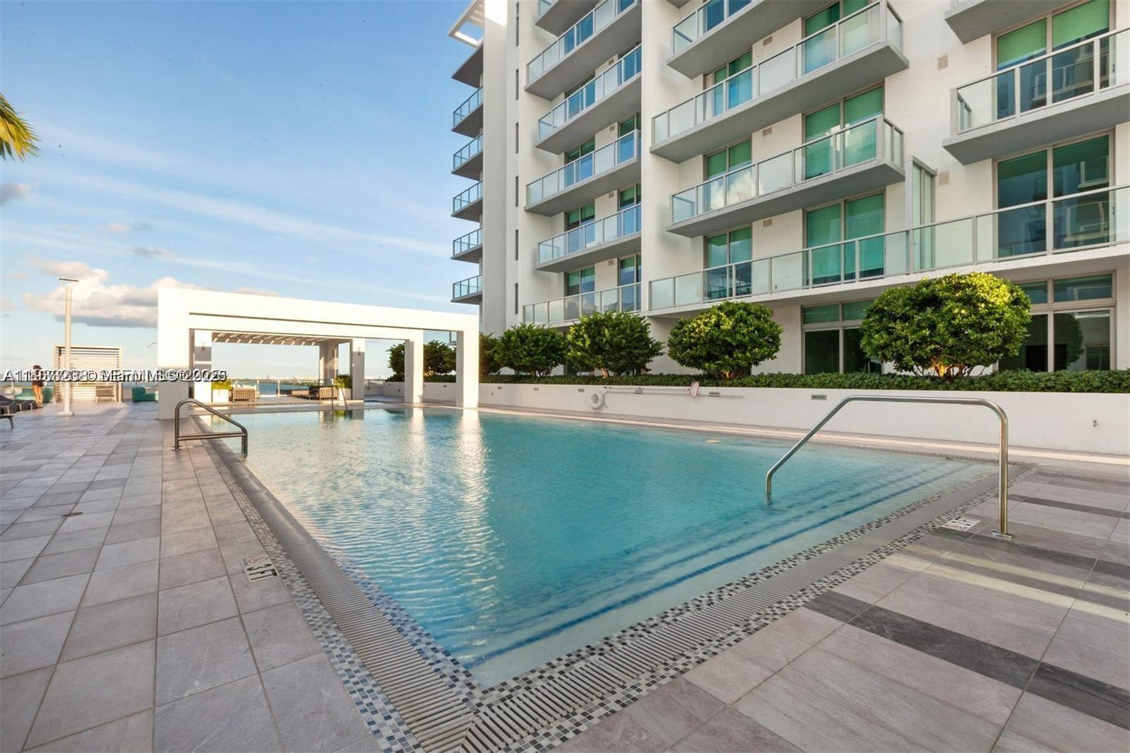 A swimming pool sits on a tiled deck next to a modern multi-story apartment building — 3900 Biscayne Blvd # 905, Miami FL 33137, MIAMI, FL