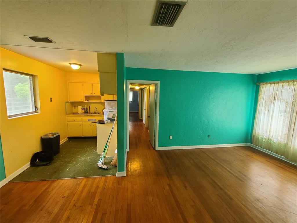A living room with hardwood floors and turquoise walls opens to a yellow kitchen area — 217 NW 36TH STREET, GAINESVILLE, FL