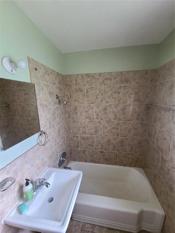 A bathroom features a white sink, a bathtub with a showerhead, and tan tiled walls — 217 NW 36TH STREET, GAINESVILLE, FL