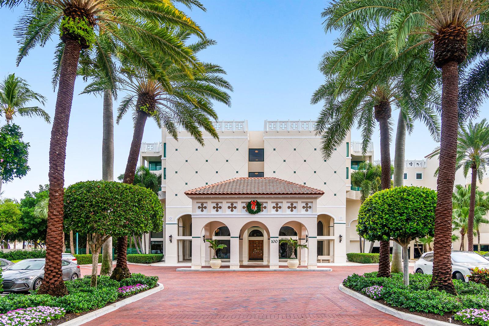 The exterior of a multi-story building features a covered entrance with palm trees and landscaping — 100 SE 5th Avenue # 410, Boca Raton FL 33432, BOCA RATON, FL