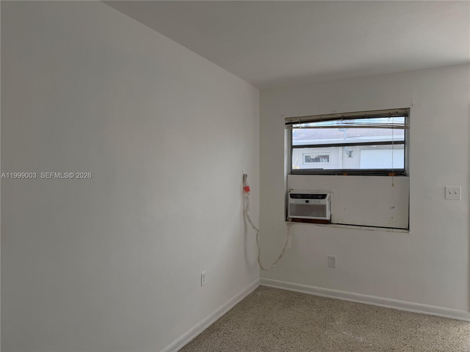 A sparse room features white walls, beige carpeting, and a window-mounted air conditioning unit — 9283 SW 39th St, Miami FL 33165, MIAMI, FL