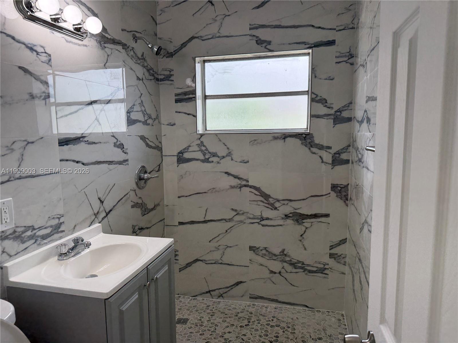 A bathroom features a gray vanity, marble-patterned wall tiles, and a walk-in shower area — 9283 SW 39th St, Miami FL 33165, MIAMI, FL