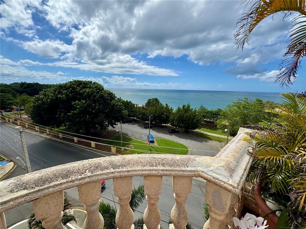 A view from a stone balcony overlooking a parking lot, trees, and the ocean — Cambija CALLE CAMBIJA UNIT 401, RINCON, PR