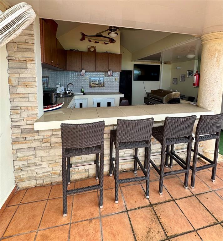 An outdoor kitchen features a tiled bar with four wicker stools and stone wall accents — Cambija CALLE CAMBIJA UNIT 401, RINCON, PR