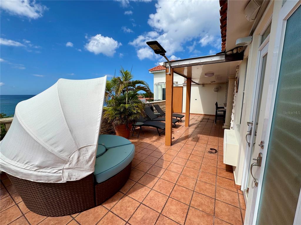 A tiled outdoor terrace features a round daybed, lounge chairs, and a partial roof covering — Cambija CALLE CAMBIJA UNIT 401, RINCON, PR