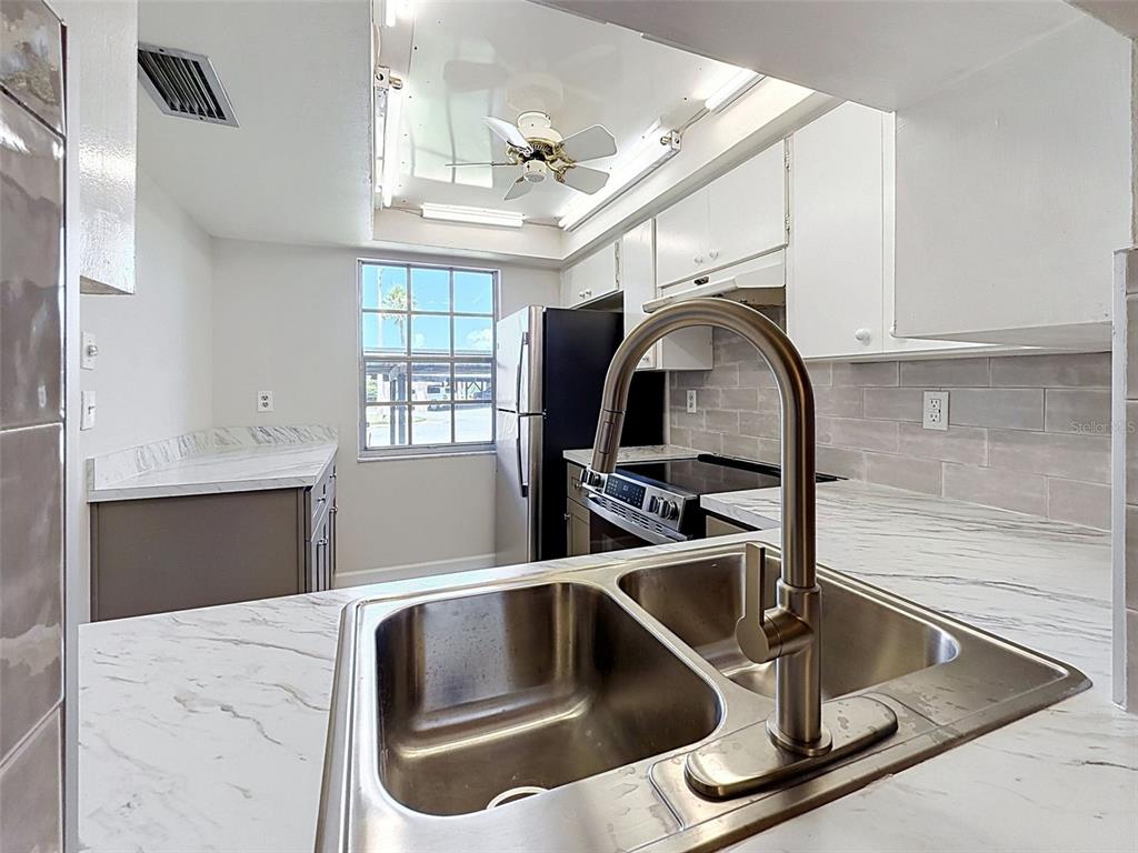 A kitchen features white upper cabinets, gray lower cabinets, stainless steel appliances, and tiled flooring — 4422 SUNSTATE DRIVE, NEW PORT RICHEY, FL
