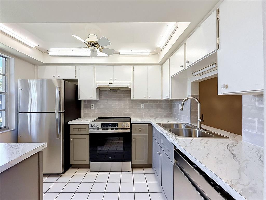 A kitchen features gray lower cabinets, white upper cabinets, a stainless dishwasher, and tile flooring — 4422 SUNSTATE DRIVE, NEW PORT RICHEY, FL