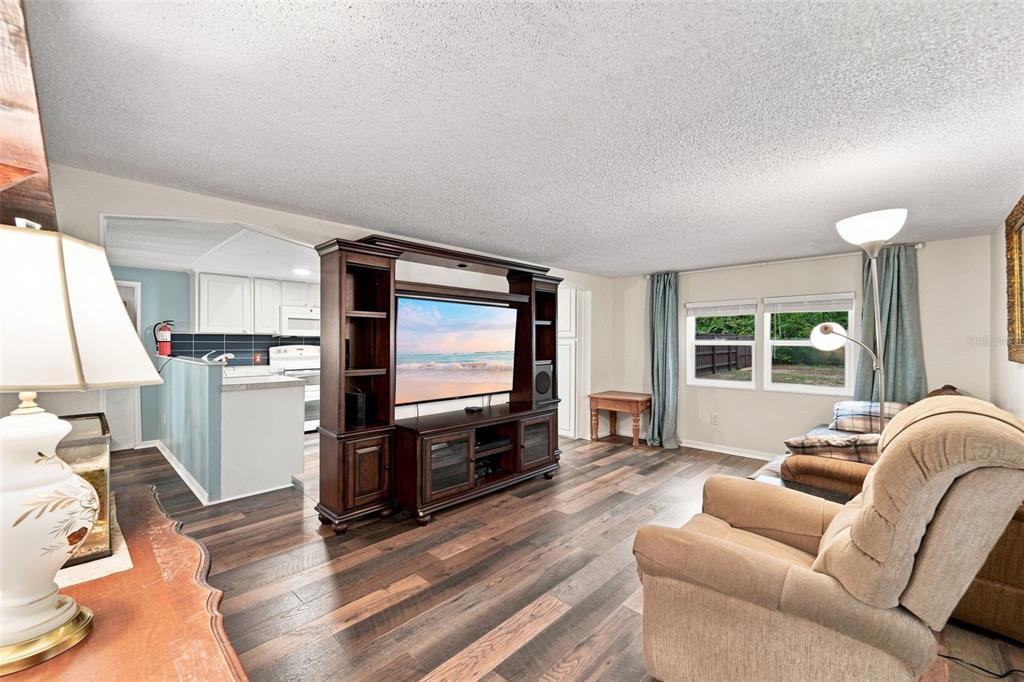 A living room with wood-look flooring, a large entertainment center, and an adjacent kitchen area — 31622 ANOTHER ANNA ROAD, DELAND, FL