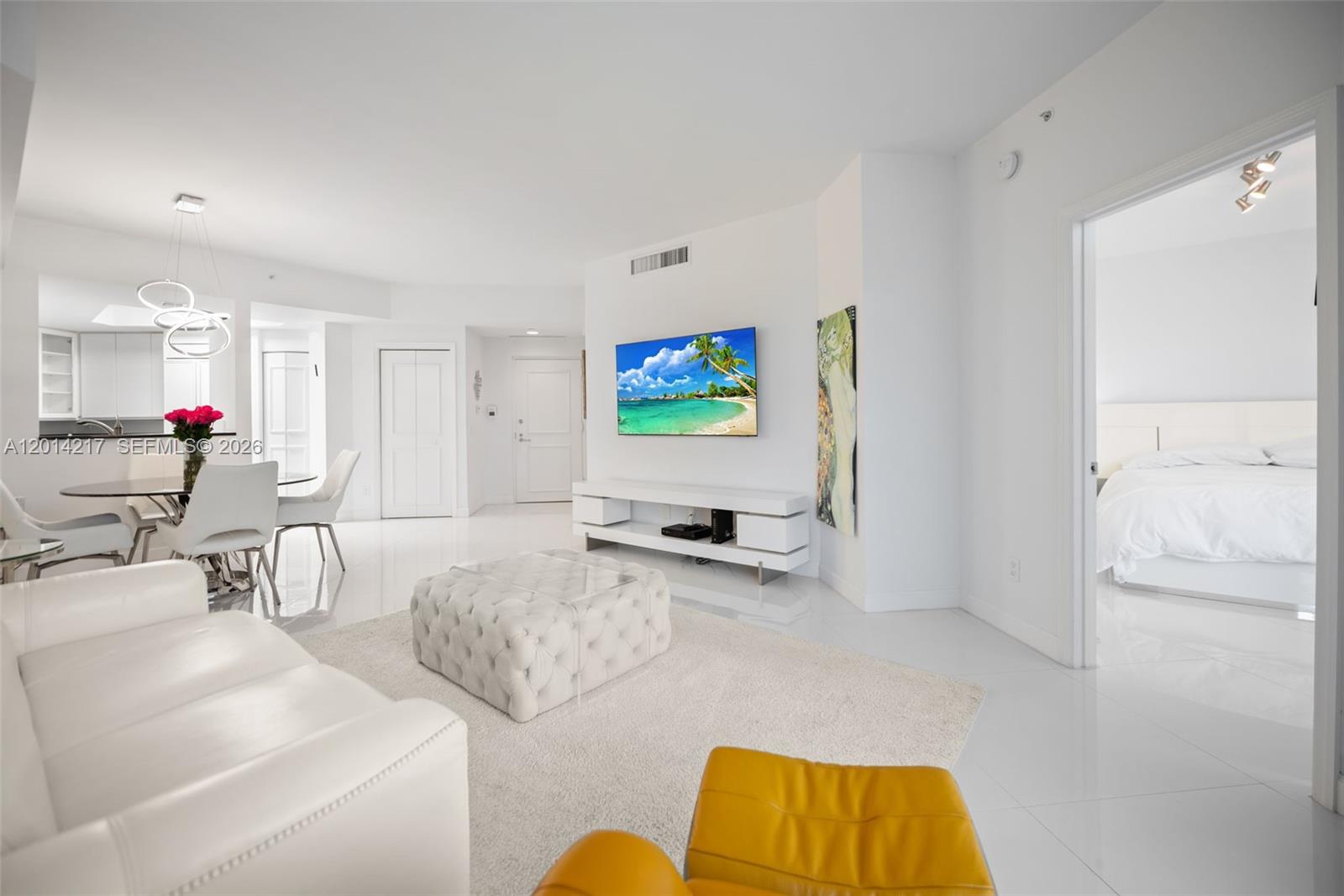 A bright living room features white tile floors, a white sofa, and a wall-mounted television — 21050 Point Pl # 302, Aventura FL 33180, AVENTURA, FL