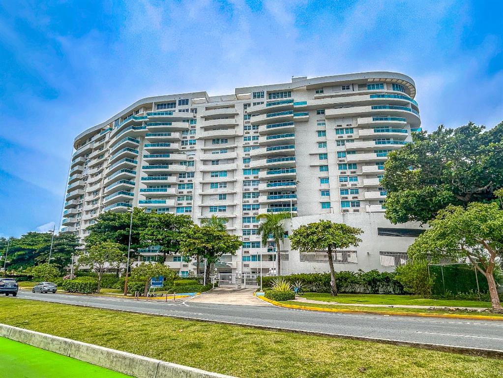 A multi-story white residential building with curved balconies stands behind a paved road and lawn — 550 AVENIDA CONSTITUCION UNIT 810, SAN JUAN, PR