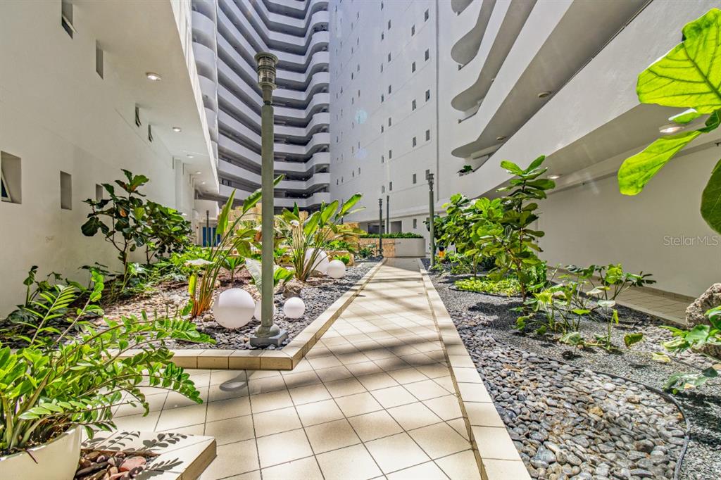 A paved walkway leads through a landscaped courtyard between two tall white residential buildings — 550 AVENIDA CONSTITUCION UNIT 810, SAN JUAN, PR