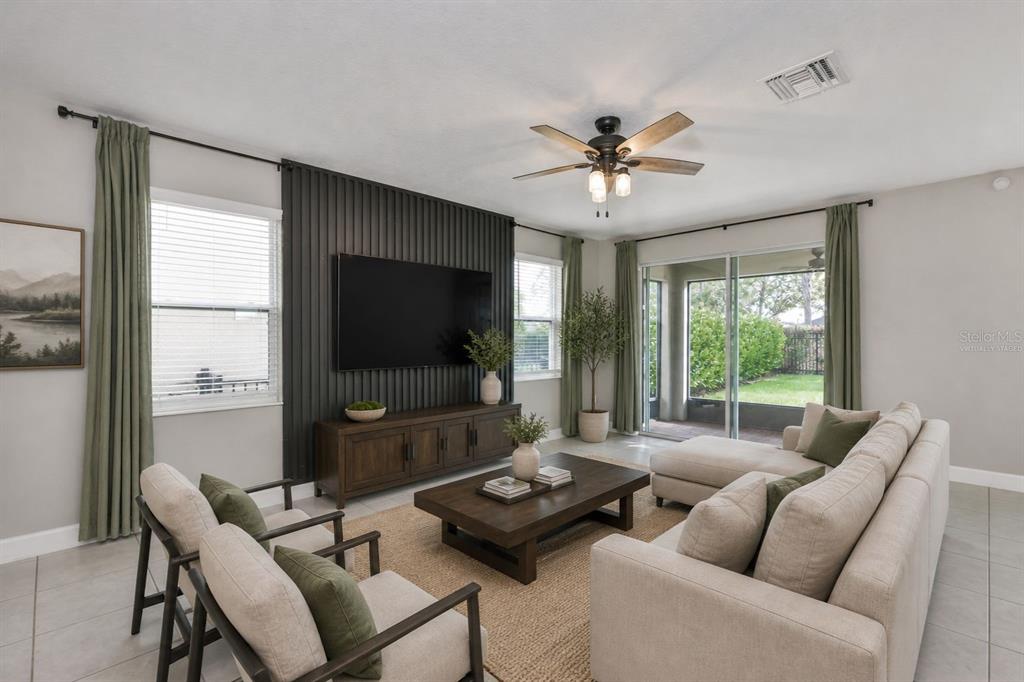 A living room features a dark wood-slatted accent wall, a television, and neutral-toned furniture — 6207 VOYAGERS PLACE, APOLLO BEACH, FL