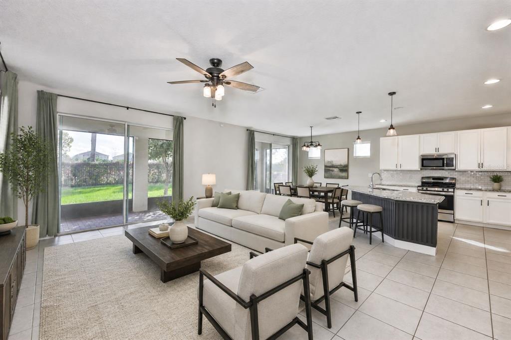 An open-concept living room and kitchen feature tile floors, a ceiling fan, and sliding doors — 6207 VOYAGERS PLACE, APOLLO BEACH, FL