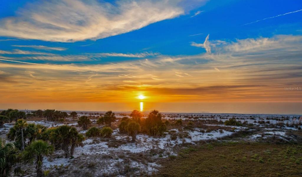 A sunset view over a sandy beach with palm trees and dunes in the foreground — 1040 ELDORADO AVENUE, CLEARWATER BEACH, FL